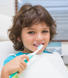 Little boy in dentists chair using toothrbrush at the dental clinic